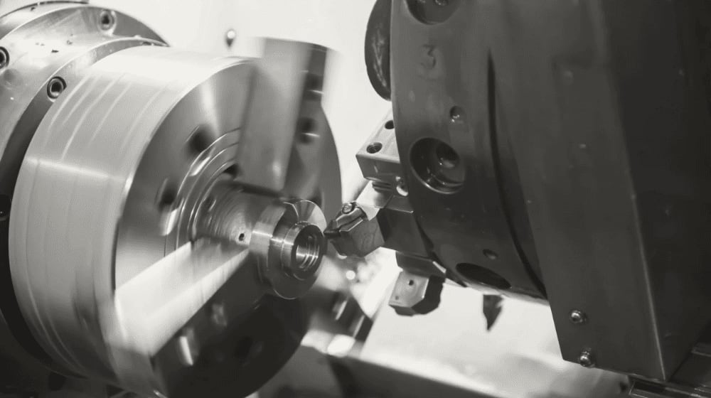 Tornio CNC in funzione che lavora un pezzo metallico rotante con un utensile da taglio, evidenziando il processo di fabbricazione di precisione.