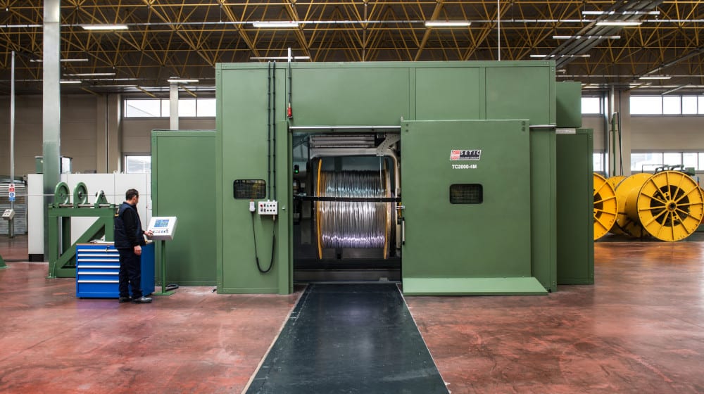 Worker operating a large SETIC TC2000-4M industrial machine with a full spool of metallic wire in a manufacturing plant.