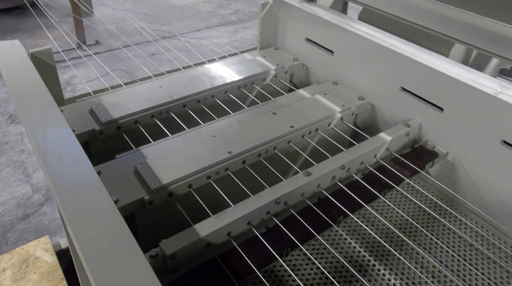 Industrial wire processing machine showing multiple thin, parallel wires fed through a series of grey guiding mechanisms.