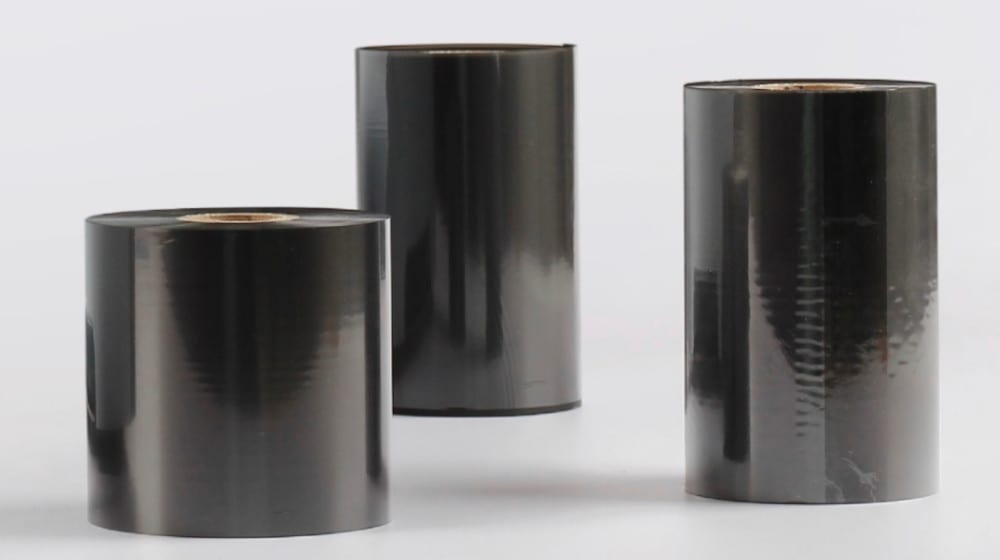 Tre bobine di nastro nero a trasferimento termico lucido per stampanti di etichette, su sfondo bianco.