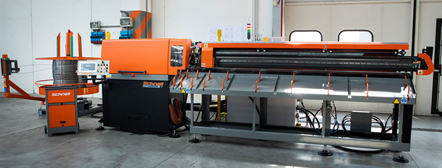 Schnell automatic rebar processing machine, featuring a large wire coil feeder on the left and a long straightening and cutting unit on the right, in a factory setting.