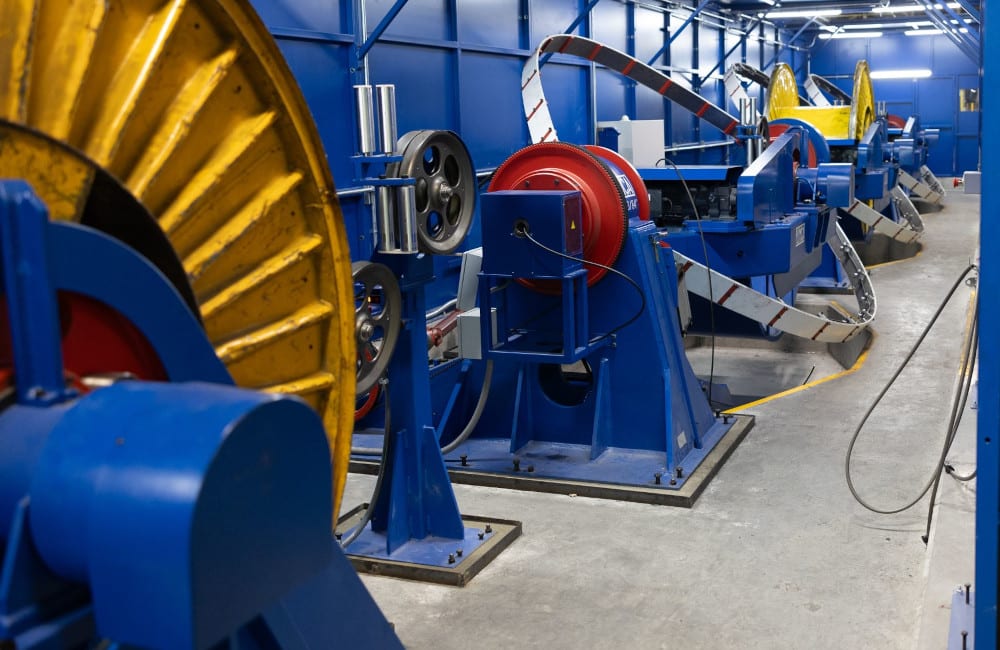 Long line of blue and yellow industrial machinery for cable or wire processing, featuring large spools, in a factory.
