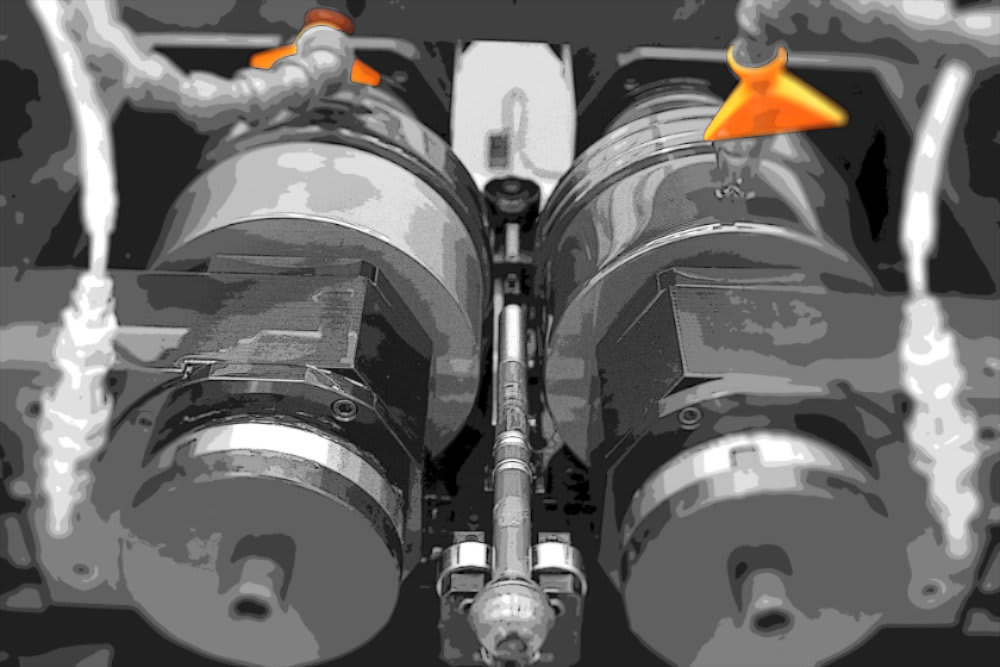 Macchinario industriale con due rulli paralleli, asta metallica centrale e ugelli che erogano liquido di raffreddamento.