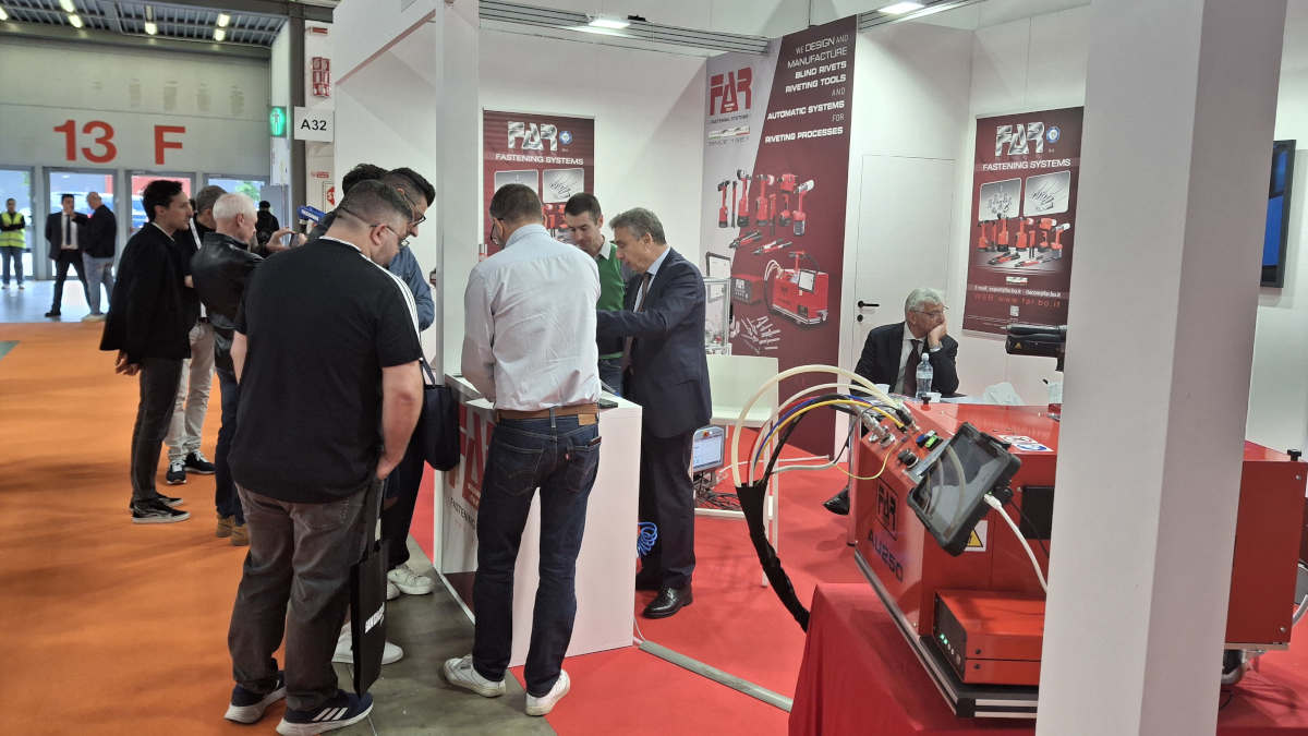 People interacting at a FAR Fastening Systems trade show booth, showcasing blind rivets, riveting tools, and automatic systems for riveting processes.