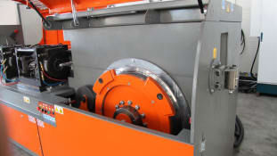Máquina industrial de enderezado y corte de alambre con gran disco giratorio naranja y carcasa gris.