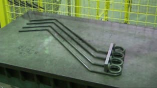 Quatre éléments chauffants industriels en tubes métalliques pliés avec des bobines spirales, posés sur une table d'atelier.