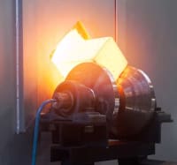 Lingotto metallico quadrato incandescente in lavorazione ad alta temperatura su macchinario industriale.