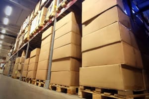 Ampio magazzino di stoccaggio con lunghe file di scaffali industriali carichi di scatole di cartone impilate su pallet.