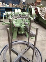 Industrial green nail making machine processing metal wire from a large spool on a factory floor.