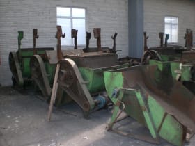 A row of large, green heavy-duty industrial processing machines with trough-like bodies and vertical components, showing signs of wear and rust, on a factory floor.