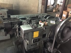 Grey industrial production machine with a control panel, yellow label, and a large drive wheel connected by a belt system.