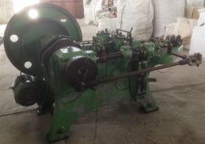 Large green industrial nail making machine with a prominent flywheel on the left and multiple processing stations.