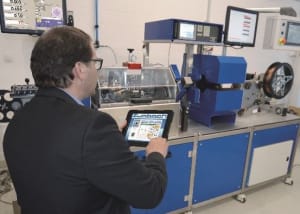 Man in a suit operating industrial testing machinery with a tablet in a laboratory setting.