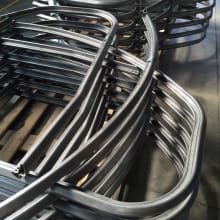 Pile di tubi metallici curvati, elementi per telai o componenti industriali, su pallet in un ambiente di produzione.
