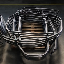 Pila di tubi metallici piegati a U su un pallet di legno, componenti industriali pronti per la lavorazione.