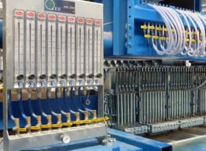 SKF centralized lubrication control system featuring nine individual flow meters with manual adjustment valves, integrated with a large industrial machine's numerous lubrication points and white hoses.