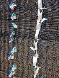 Pannelli di rete elettrosaldata arrugginiti impilati, legati con cinghie bianche e con etichette identificative blu sul lato sinistro.