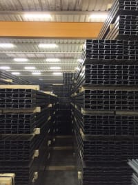 Aisle in an industrial warehouse featuring high stacks of dark steel channels and metal profiles.