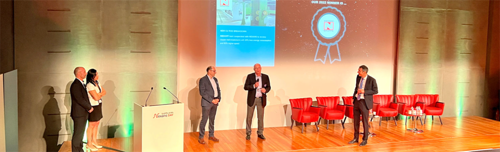 Evento Nexans Suppliers Day con relatori su palco, podio e schermo che celebra un vincitore del 2022 e le innovazioni Nexans nel risparmio energetico.