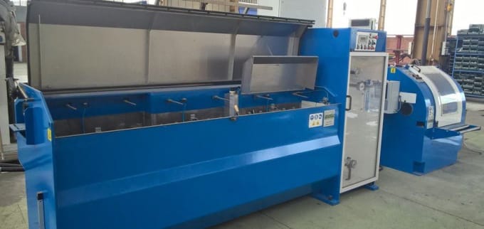 Blue industrial surface treatment or cleaning machinery with multiple open tanks and a control unit, positioned in a manufacturing factory workshop.