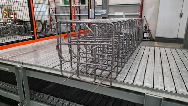 Cages d'armature en acier préfabriquées pour le béton, alignées sur une plate-forme de convoyage dans un atelier de fabrication industriel.