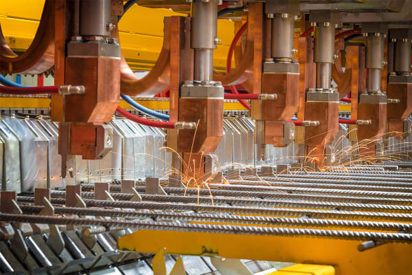 Industrial resistance welding machine actively joining metal rebar rods with multiple copper electrodes, emitting bright sparks during fabrication.