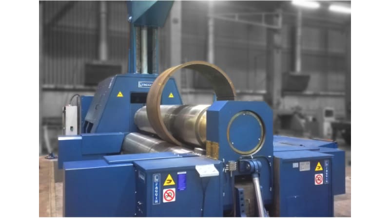 Blue Faccin industrial plate rolling machine actively bending a thick metal sheet into a large cylindrical form.