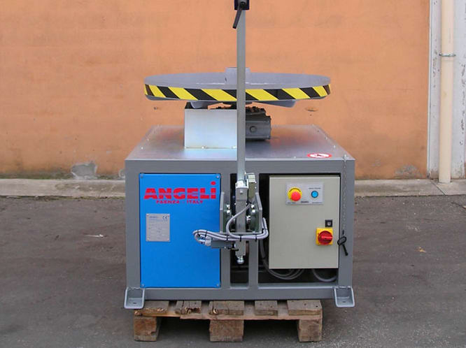 Angeli industrial machine with a grey main body, a rotating platform featuring yellow and black hazard stripes, and an electrical control panel with red and blue buttons. The machine is branded 'ANGELI PARNER ITALY' on a blue panel and sits on a wooden pallet.