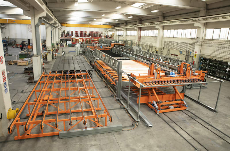 Automated industrial production line featuring orange and silver conveyor systems and processing machinery in a clean factory environment.