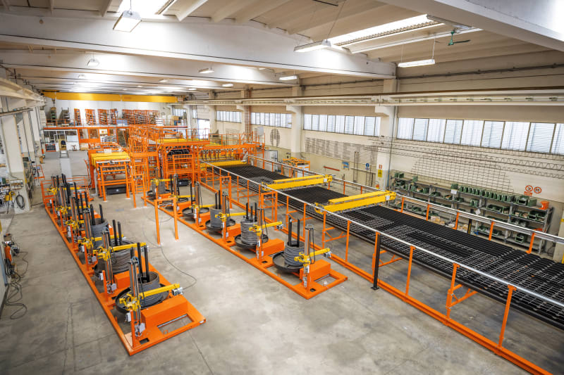 Modern industrial factory with orange automated wire processing machinery and spools of steel wire on a production line.