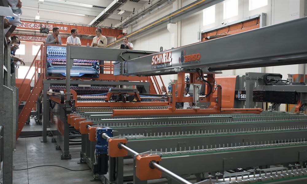 Machine industrielle Schnell Versa Line TB 250 avec logo Senso, une ligne de production automatisée observée par des hommes sur une plateforme dans une usine.