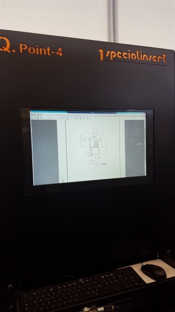 Stazione di lavoro con monitor che mostra un disegno tecnico di un inserto meccanico. Sul pannello nero superiore sono incisi i marchi Q. Point-4 e specialinsert, con tastiera e mouse in primo piano.