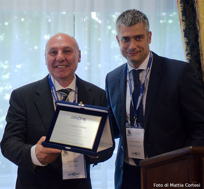 L'ingegnere Angelo Cortesi, sorridente in completo, riceve una targa premio ANCEM da Francesco Iavern durante una premiazione Expometals.