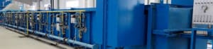 Blue industrial processing line with pipes and control panels in a factory setting