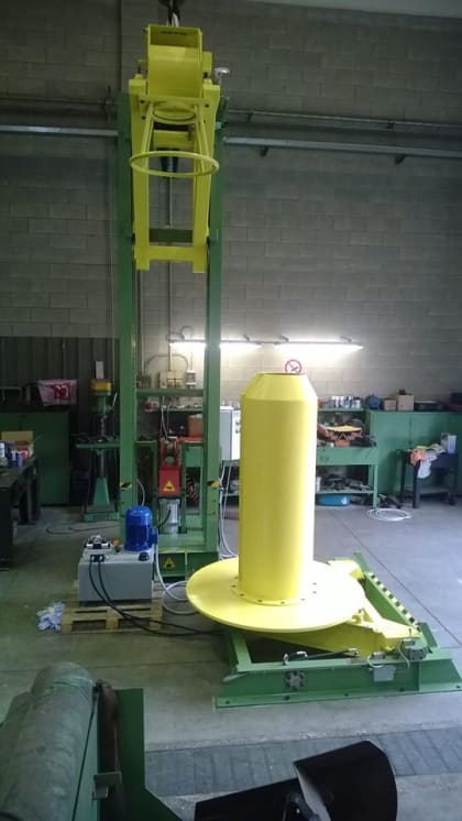 Grande macchinario industriale giallo e verde, con un sistema di sollevamento o movimentazione superiore e una stazione di bobinatura o svolgimento inferiore, situato in un'officina.