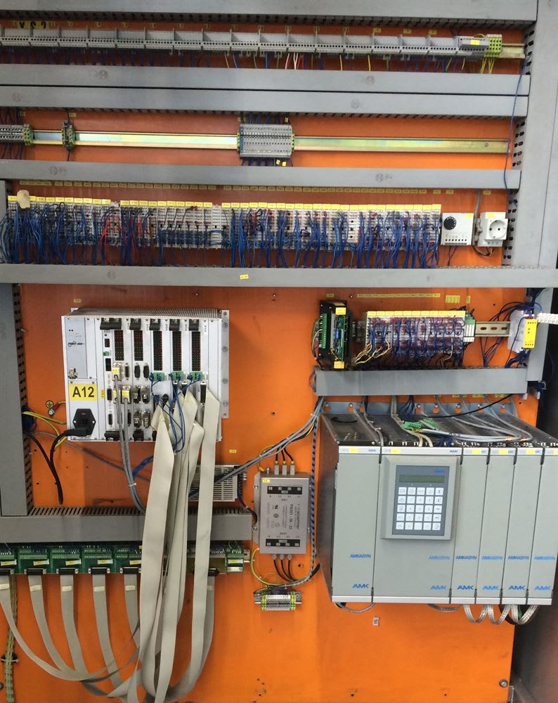 Industrial control panel featuring AMKADYN servo drives, a multi-module PLC system, and organized industrial wiring on an orange backboard.