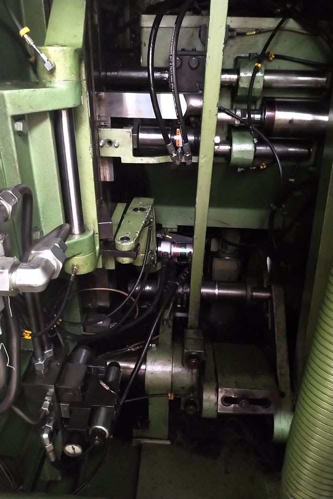 Interior view of a heavy industrial machine, featuring green metal components, multiple hydraulic cylinders, control valves, and a dense network of connected hoses.