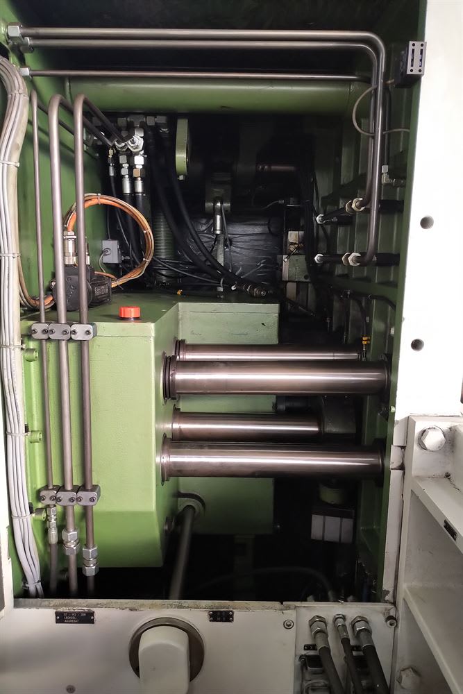 Internal view of industrial machinery with green housing, revealing a complex hydraulic system, electrical wiring, and large metal cylinders.