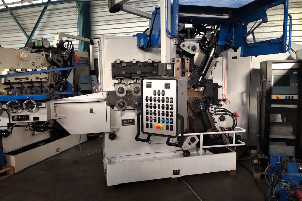 Wafios industrial wire forming machine with an operator control panel and multiple processing rollers in a factory.