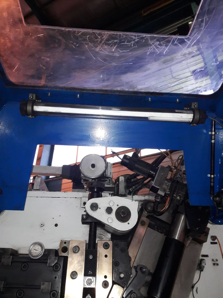 Industrial machine interior showing a clear, scratched safety shield, a fluorescent light, a pressure gauge, and intricate metal mechanical components.