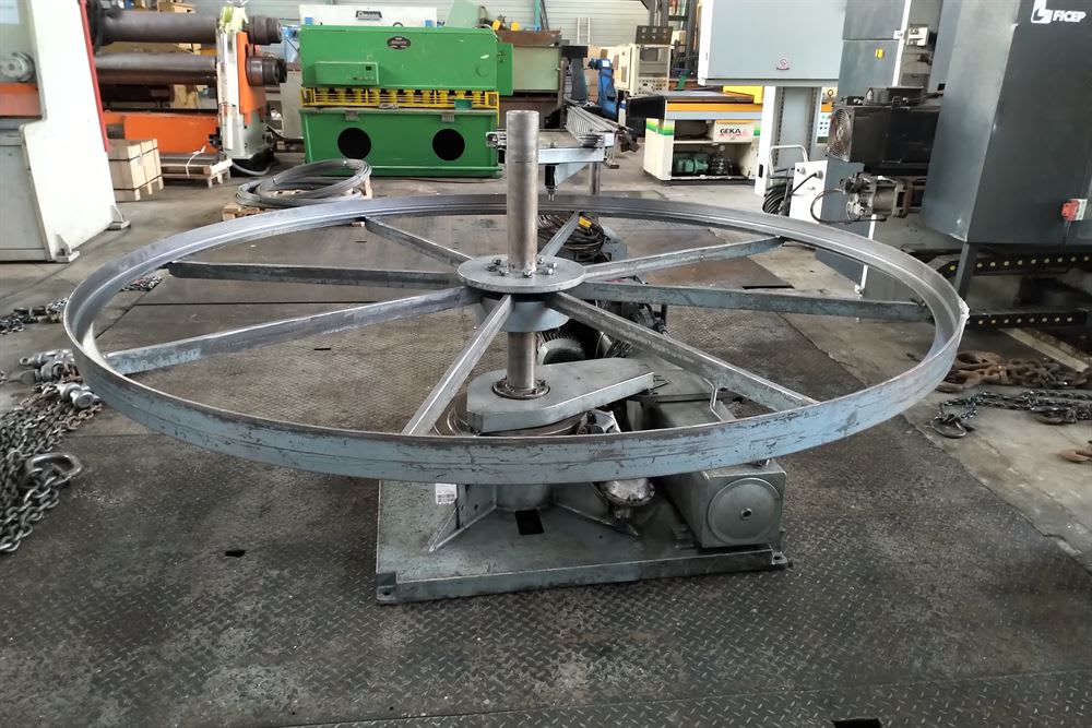 Large steel industrial reel or wheel on a rotating fabrication stand in a metalworking workshop.
