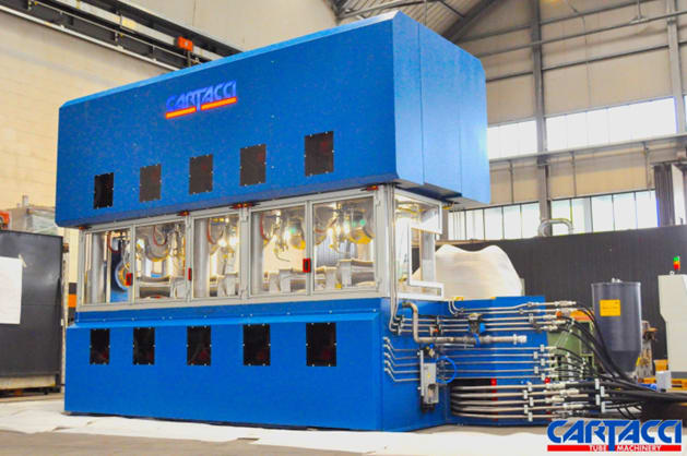 Large blue Cartacci tube manufacturing machine with observation windows showing internal mechanisms and complex external piping, situated in a brightly lit factory.