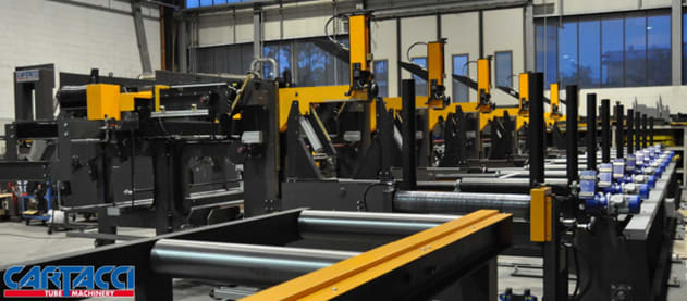 Lunga linea di macchinari industriali Cartacci per la lavorazione di tubi, con stazioni multiple, elementi gialli e rulli trasportatori in uno stabilimento.