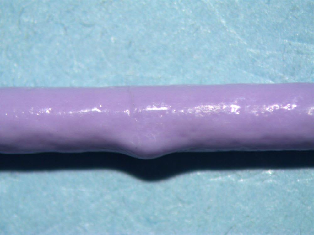 Gros plan d'un tube cylindrique violet présentant une légère dépression sur sa face inférieure, posé sur un fond bleu texturé.