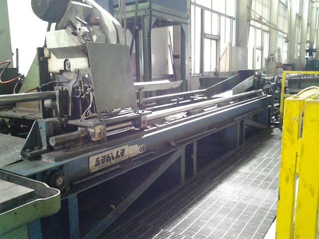 SEGAL industrial metal cutting machine with a long conveyor system processing metal tubes or rods, located in a manufacturing plant with a grated floor.