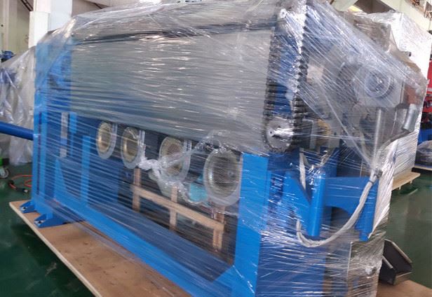 Blue industrial machinery, stretch-wrapped in clear plastic for shipment, resting on a wooden pallet.