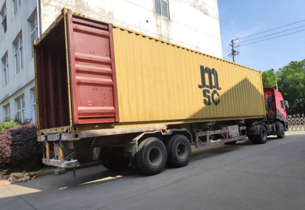 Yellow MSC shipping container on a red semi-truck trailer, with its rear door open, parked next to a white building.