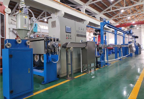 Industrial cable and wire extrusion production line with a material hopper, central control panel, and a long blue cooling section in a factory with a green floor.