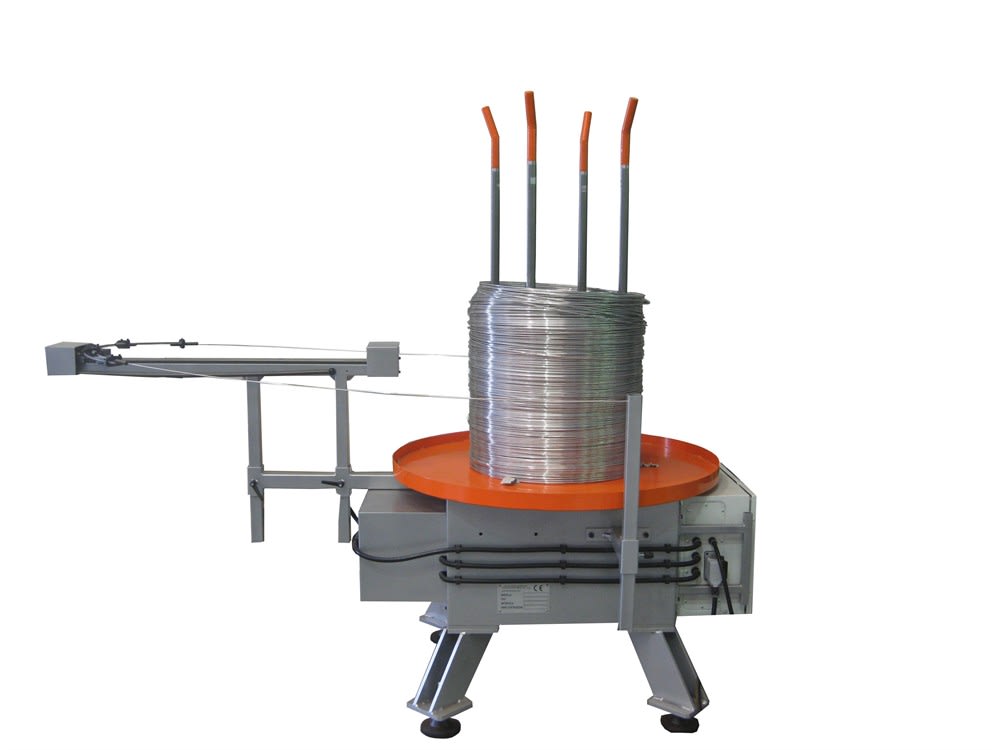 Macchina svolgifilo industriale con grande bobina di filo metallico argentato su piattaforma arancione rotante e braccio di guida orizzontale.