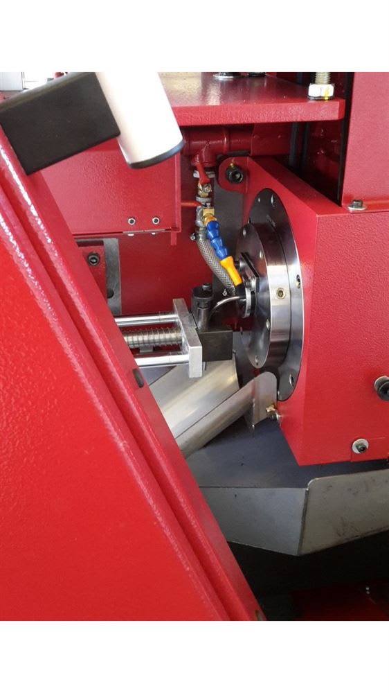 Macchinario industriale rosso per lavorazione meccanica di precisione, con pezzo montato sul mandrino e ugelli per liquido refrigerante.